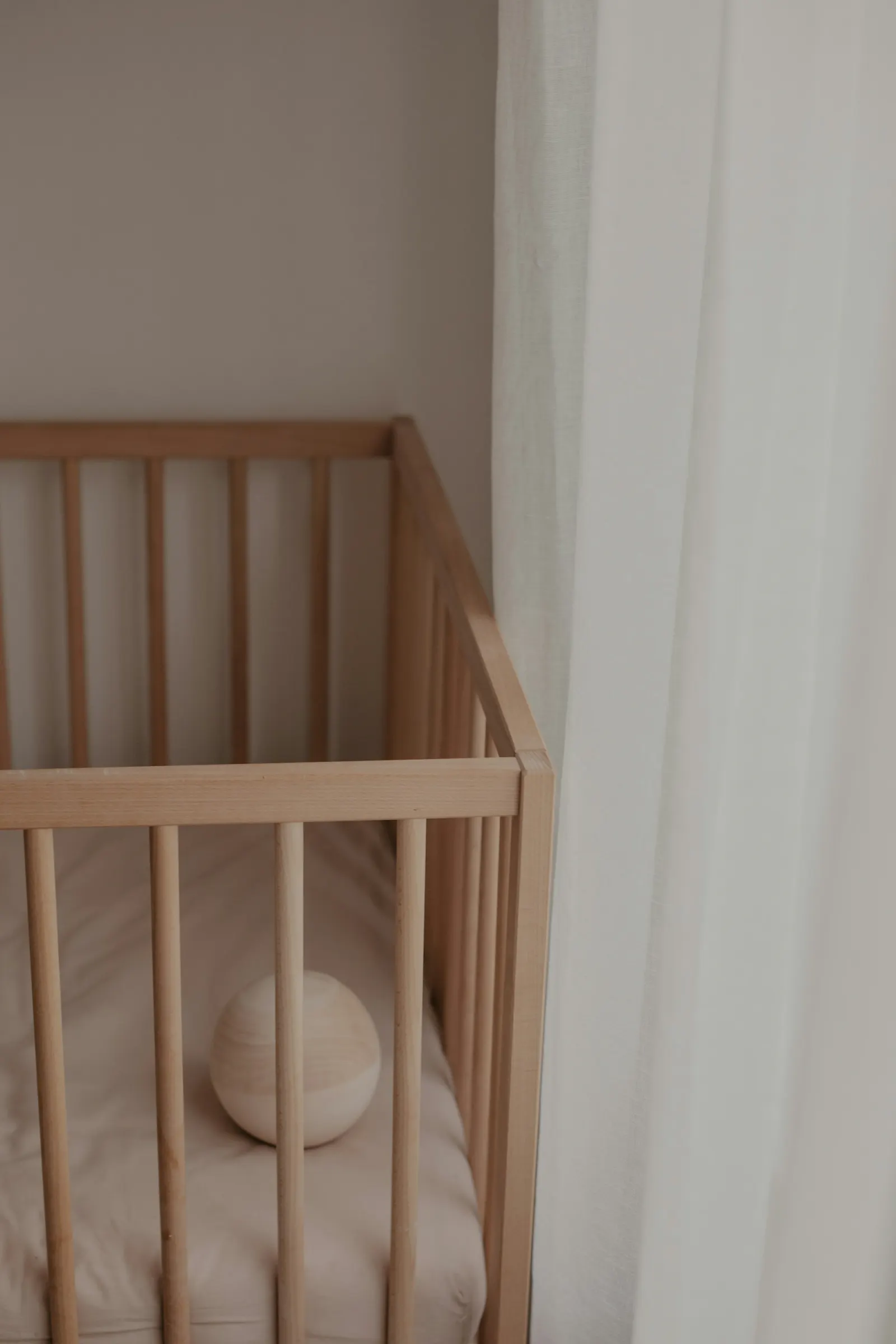Een houten ledikantje in een rustige hoek bij een licht gordijn